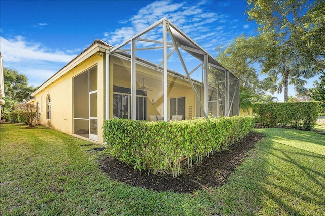 view of property exterior with a lawn, ceiling fan, and glass enclosure