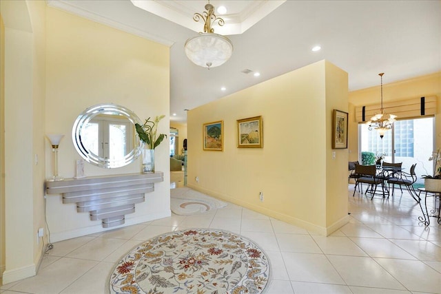 entrance foyer with a tray ceiling, light tile patterned floors, a notable chandelier, and ornamental molding