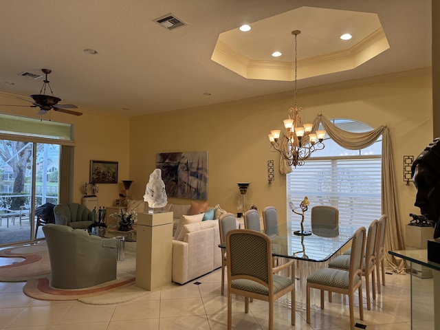 tiled dining space featuring ceiling fan with notable chandelier, a tray ceiling, and ornamental molding