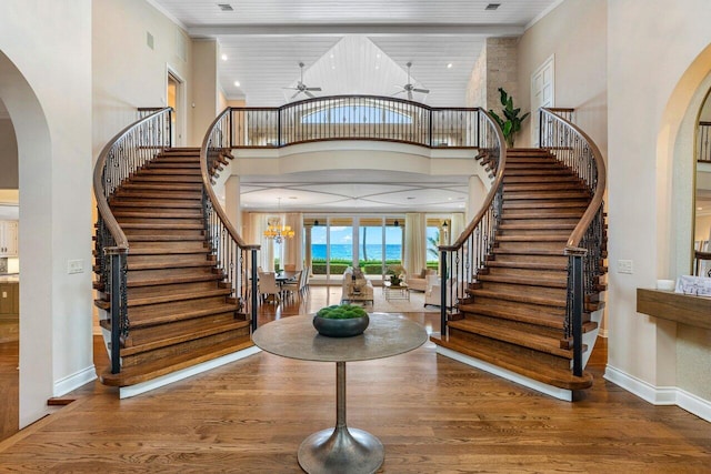 foyer featuring wood-type flooring, ceiling fan with notable chandelier, and a high ceiling