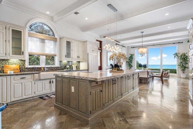 kitchen featuring a kitchen island, decorative light fixtures, backsplash, a water view, and beam ceiling