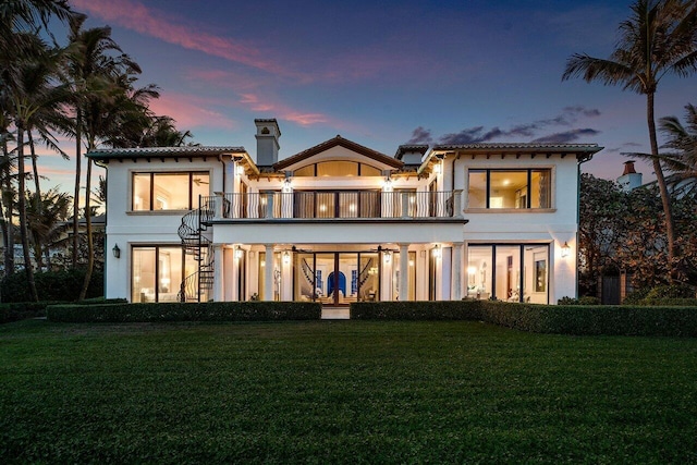 back house at dusk with a balcony and a yard