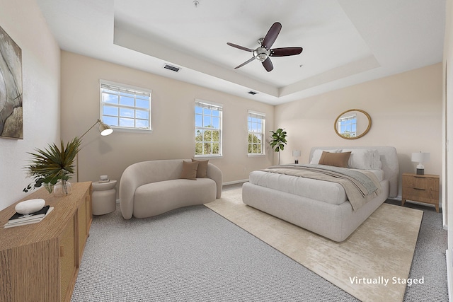 carpeted bedroom featuring visible vents, baseboards, a raised ceiling, and ceiling fan