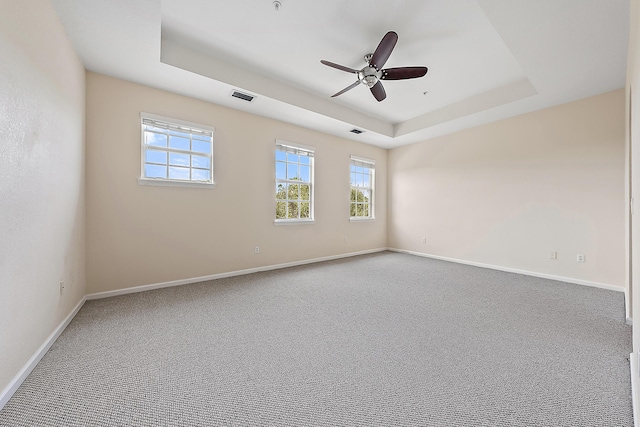 carpeted empty room with visible vents, ceiling fan, baseboards, and a tray ceiling