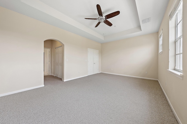 carpeted empty room with baseboards, a tray ceiling, arched walkways, and visible vents