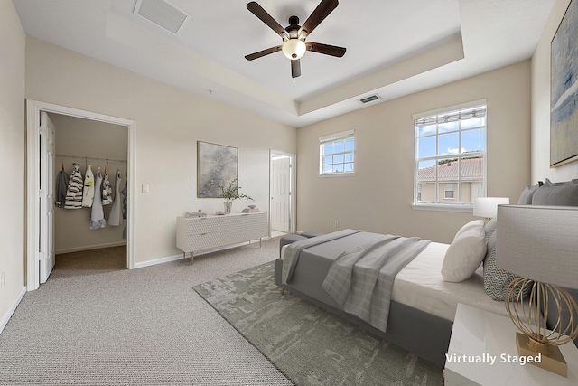 bedroom with a walk in closet, carpet floors, a closet, a raised ceiling, and ceiling fan