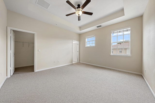 unfurnished bedroom featuring ceiling fan, carpet, a tray ceiling, and a walk in closet