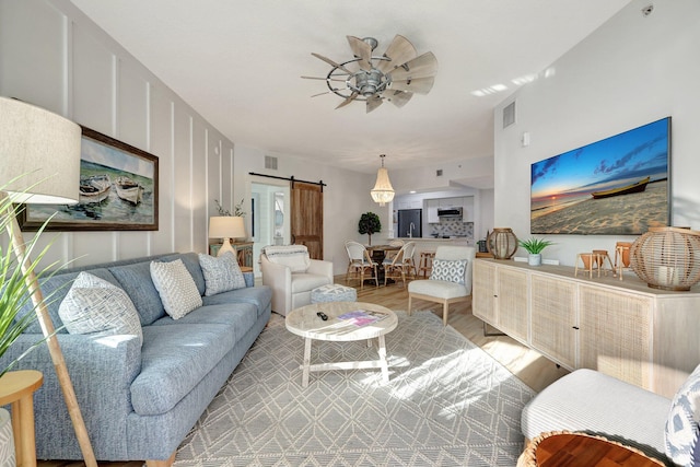 living room featuring ceiling fan, light hardwood / wood-style floors, and a barn door