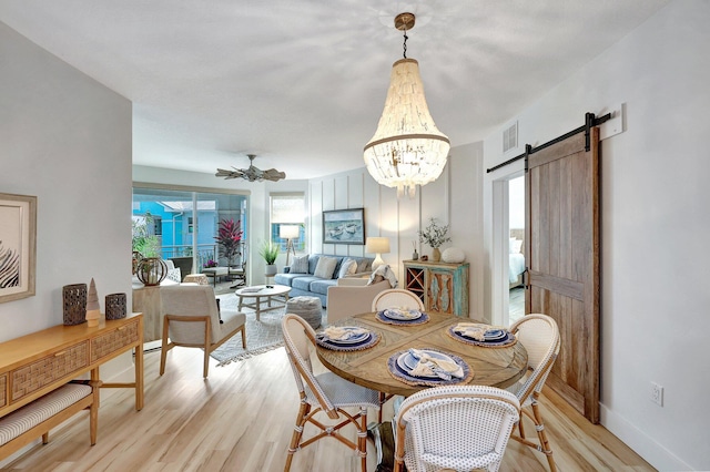 dining area with a barn door, ceiling fan with notable chandelier, and light hardwood / wood-style floors