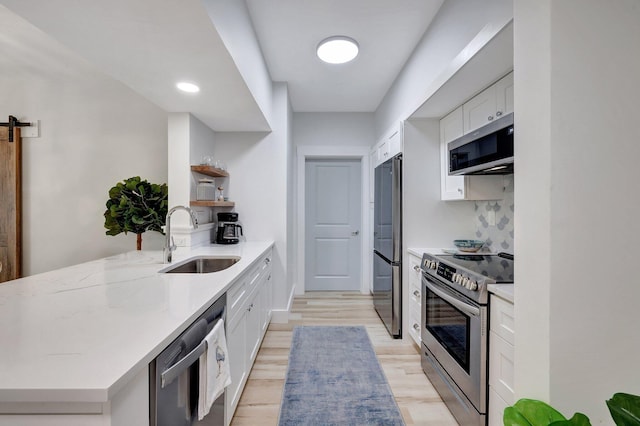 kitchen with white cabinetry, a barn door, stainless steel appliances, light stone countertops, and sink