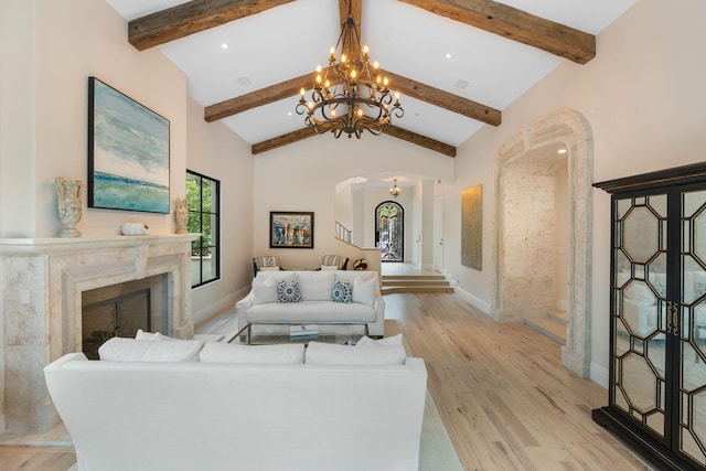 living room with a premium fireplace, a chandelier, light hardwood / wood-style floors, and beamed ceiling