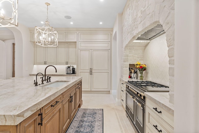 kitchen with decorative light fixtures, light stone counters, range with two ovens, and a center island with sink