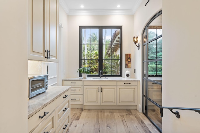 kitchen featuring sink, crown molding, cream cabinetry, and light wood-type flooring