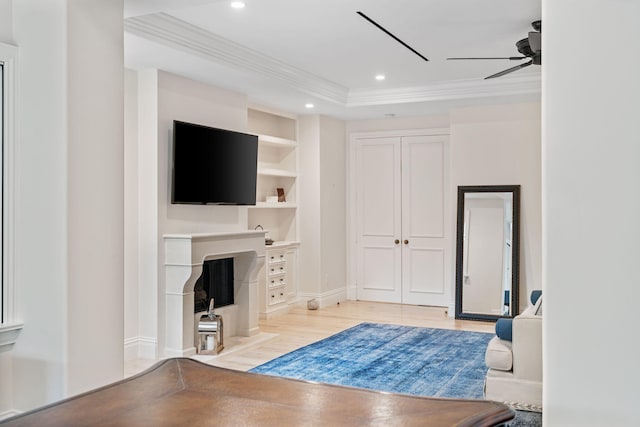 living room with ceiling fan, a tray ceiling, light wood-type flooring, ornamental molding, and built in shelves