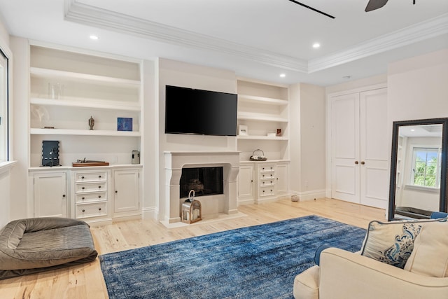 living room with a raised ceiling, ceiling fan, a tile fireplace, and light hardwood / wood-style floors