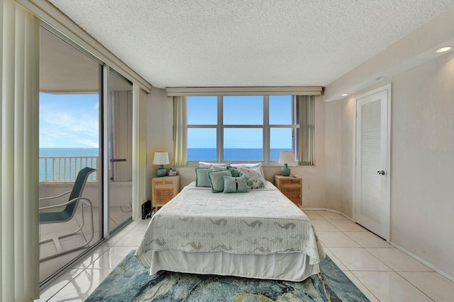 bedroom with a water view, light tile patterned floors, floor to ceiling windows, and a textured ceiling