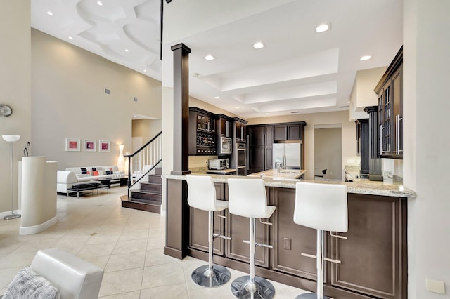 kitchen with stainless steel fridge with ice dispenser, kitchen peninsula, a breakfast bar area, a raised ceiling, and light tile patterned flooring