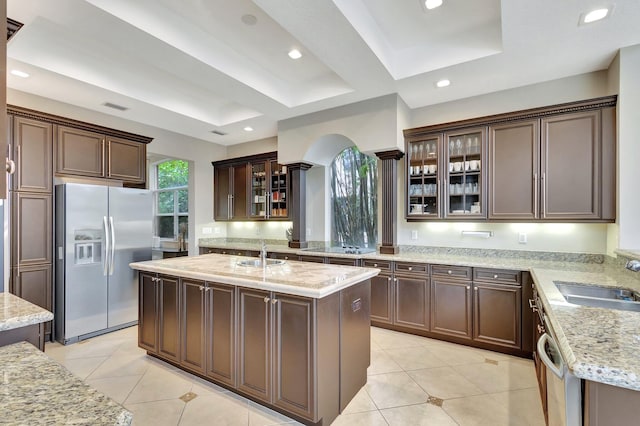 kitchen with a raised ceiling, sink, a kitchen island with sink, stainless steel appliances, and light tile patterned floors