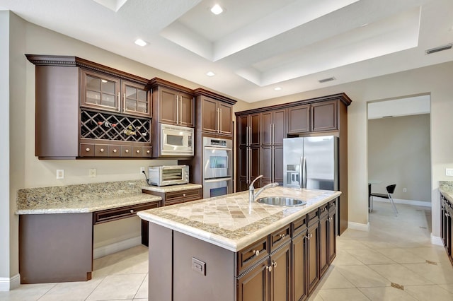 kitchen featuring a tray ceiling, stainless steel appliances, sink, a kitchen island with sink, and light tile patterned floors