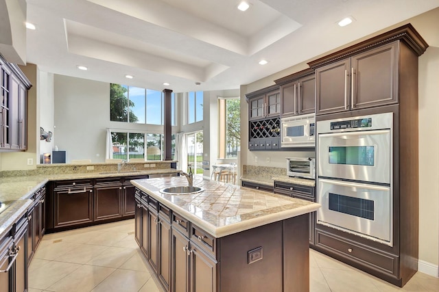 kitchen with a raised ceiling, kitchen peninsula, appliances with stainless steel finishes, and an island with sink