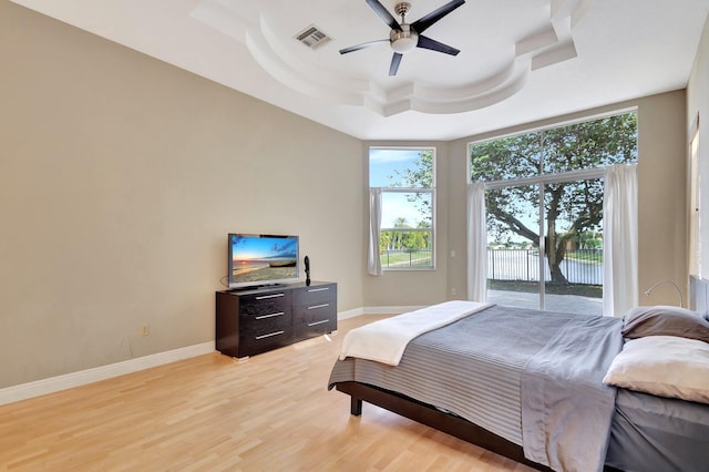 bedroom featuring ceiling fan, a raised ceiling, access to outside, multiple windows, and light wood-type flooring