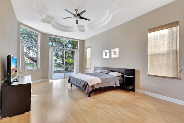 bedroom with light wood-type flooring, ceiling fan, access to exterior, and a tray ceiling