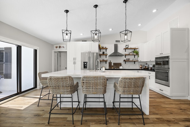 kitchen with stainless steel appliances, an island with sink, wall chimney range hood, decorative backsplash, and white cabinetry