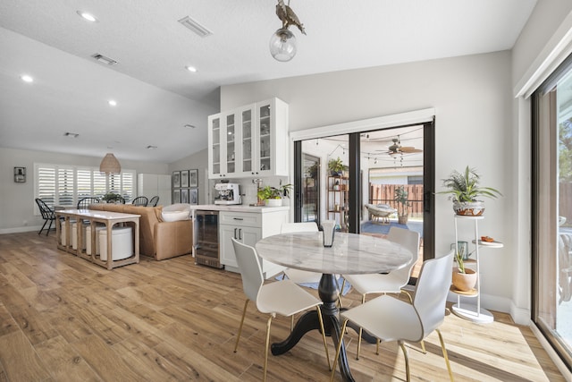 dining space with beverage cooler, light wood-type flooring, lofted ceiling, and bar