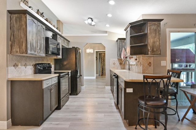 kitchen featuring a kitchen breakfast bar, dark brown cabinetry, black appliances, and vaulted ceiling