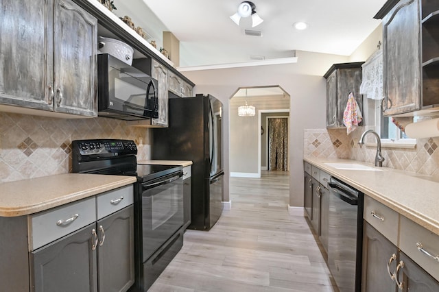 kitchen featuring pendant lighting, vaulted ceiling, black appliances, sink, and light wood-type flooring