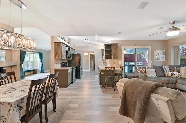 dining room featuring ceiling fan with notable chandelier, sink, and light wood-type flooring