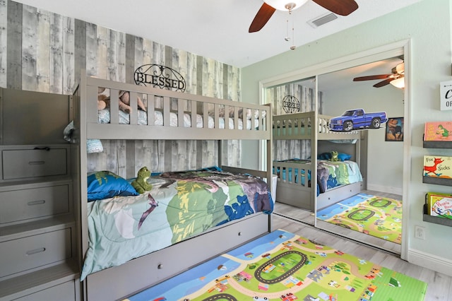 bedroom featuring ceiling fan, light wood-type flooring, a closet, and wooden walls