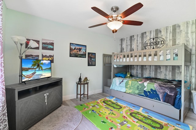 bedroom featuring ceiling fan, wood walls, and light wood-type flooring