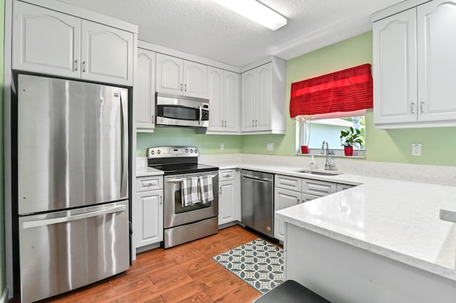 kitchen with light hardwood / wood-style floors, white cabinets, appliances with stainless steel finishes, and sink