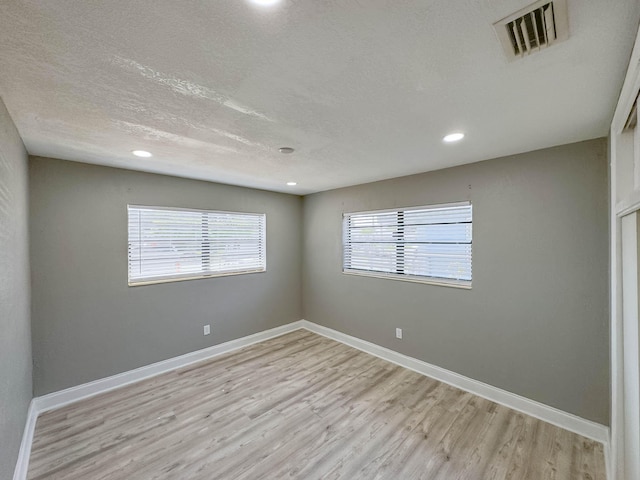 empty room with a textured ceiling and light hardwood / wood-style floors