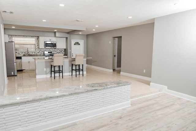 kitchen with white cabinetry, a breakfast bar area, appliances with stainless steel finishes, backsplash, and a center island