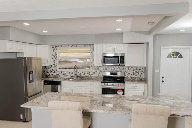 kitchen with stainless steel appliances, a kitchen breakfast bar, a kitchen island, light stone counters, and sink