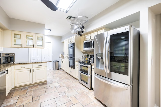 kitchen with ceiling fan, dark stone countertops, stainless steel appliances, and cream cabinets