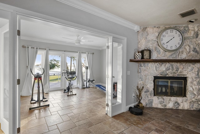 exercise room featuring crown molding, french doors, a stone fireplace, and ceiling fan