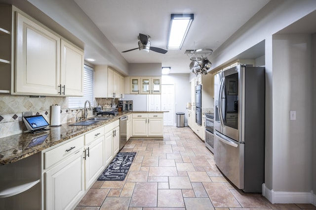 kitchen with ceiling fan, appliances with stainless steel finishes, backsplash, dark stone counters, and sink