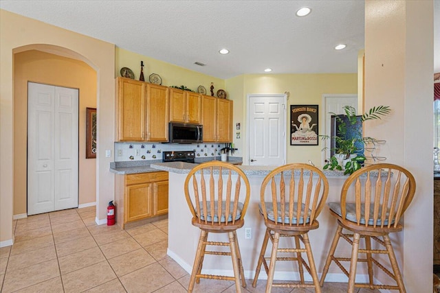 kitchen featuring a breakfast bar, light tile patterned floors, tasteful backsplash, a textured ceiling, and black range with electric stovetop