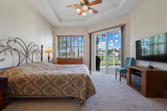 carpeted bedroom with ceiling fan, access to outside, and a tray ceiling