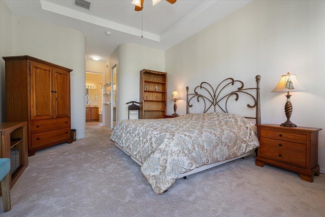 bedroom featuring ceiling fan, light colored carpet, a tray ceiling, and ensuite bath