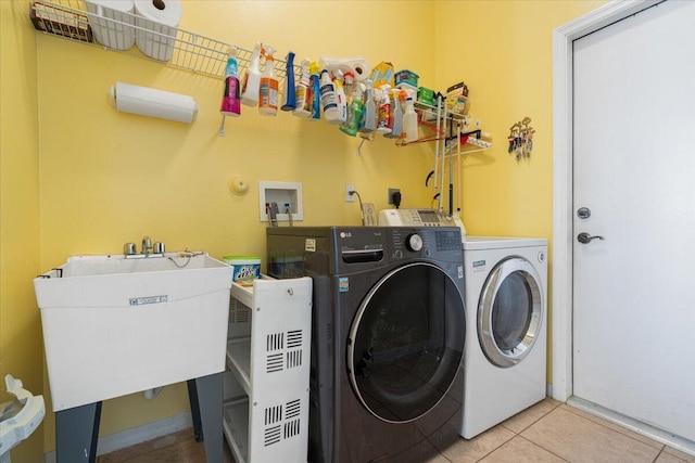 laundry area featuring light tile patterned floors, washer and clothes dryer, and sink