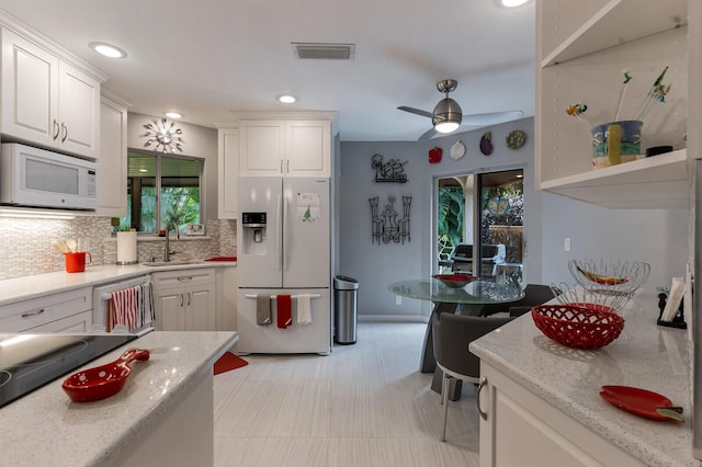 kitchen featuring white appliances, light stone counters, sink, white cabinetry, and backsplash