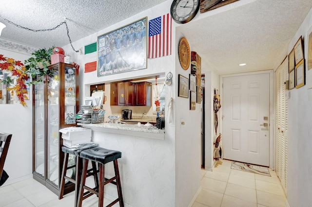 kitchen with light tile patterned floors, a kitchen breakfast bar, kitchen peninsula, and a textured ceiling