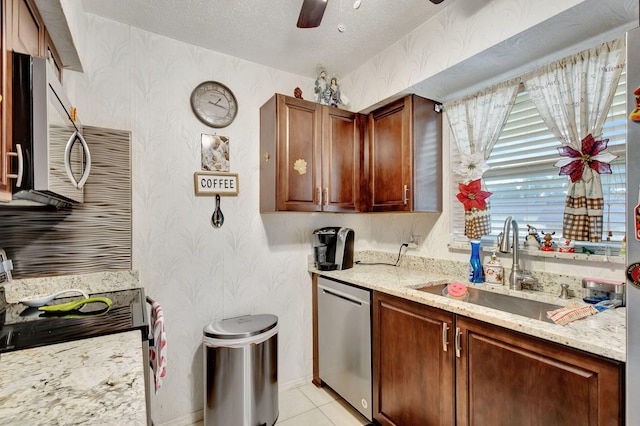 kitchen with sink, ceiling fan, appliances with stainless steel finishes, light stone counters, and a textured ceiling