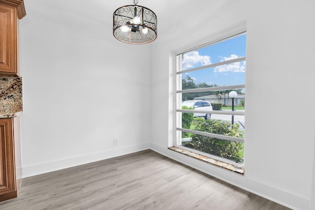 unfurnished dining area featuring an inviting chandelier and light hardwood / wood-style flooring