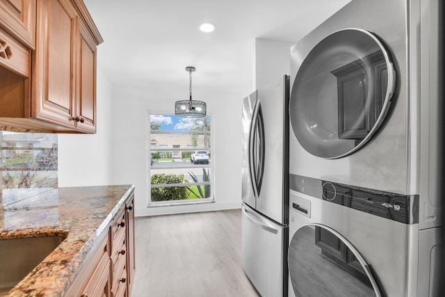 washroom featuring stacked washer and clothes dryer, light hardwood / wood-style flooring, and a chandelier