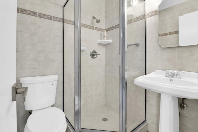 bathroom with tile walls, a shower with shower door, and toilet